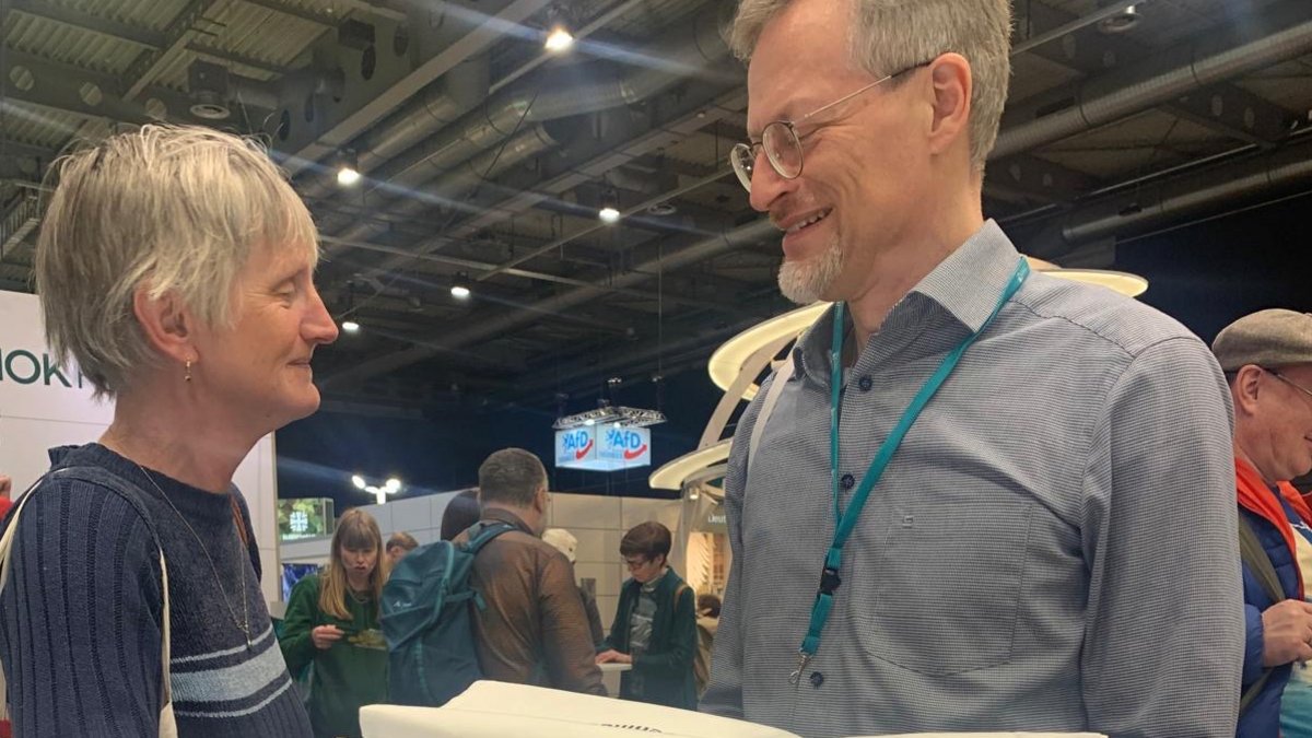 Markus Lorenz mit einer Besucherin am Infotisch des TLMB, im Vordergrund blaue Broschüren