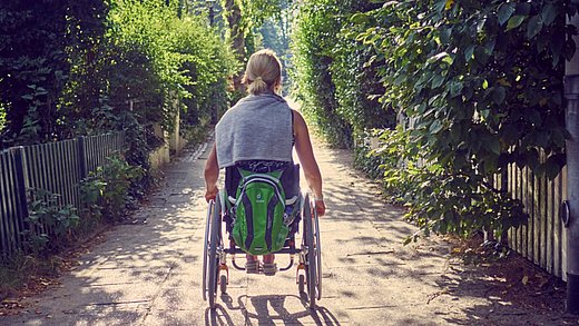 eine Rollstuhlfahrerin fährt einen Wanderweg entlang