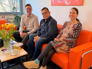 Dennis Petschner, Jens Elschner (Mitte) und Martina Beez sitzend auf der orangen Couch im Büro des TLMB, im Vordergrund ein Tischchen mit Blumen . Klick öffnet eine vergrößerte Ansicht.