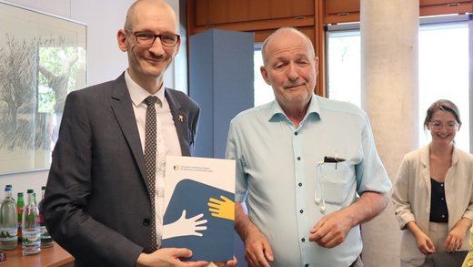 TLMB Joachim Leibiger überreicht Urkunde an Alexander Brick von der Liga Selbstvertretung, mit schwarzer Brille