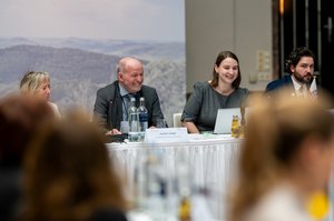 Präsidium der Konferenz mit Hintergrundbild der Tagung, Bildmitte: TLMB Leibiger und Ministerin Schenk, Bild: Jacob Schröter/TMSGAF. Klick öffnet eine vergrößerte Ansicht.