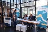 Stand im Foyer mit Besuchern und Gremienmitgliedern. Klick öffnet eine vergrößerte Ansicht.