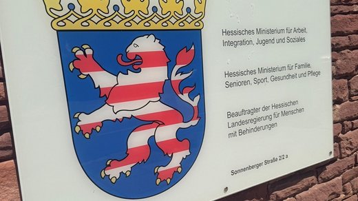 Schild an Mauer/Fassade mit dem Hessischen Landeswappen (Löwe rot-weiß auf blauem Untergrund), am Eingang zum hessischen Sozialministerium. Sitz des Hessischen Beauftragten für Menschen mit Behinderungen. 