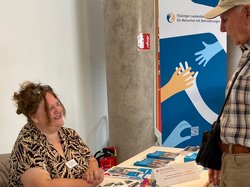 Birgit Tscherner, AGSV-Vertreterin im LBB sitzend am Info-Stand bei Beratung . Klick öffnet eine vergößerte Ansicht.